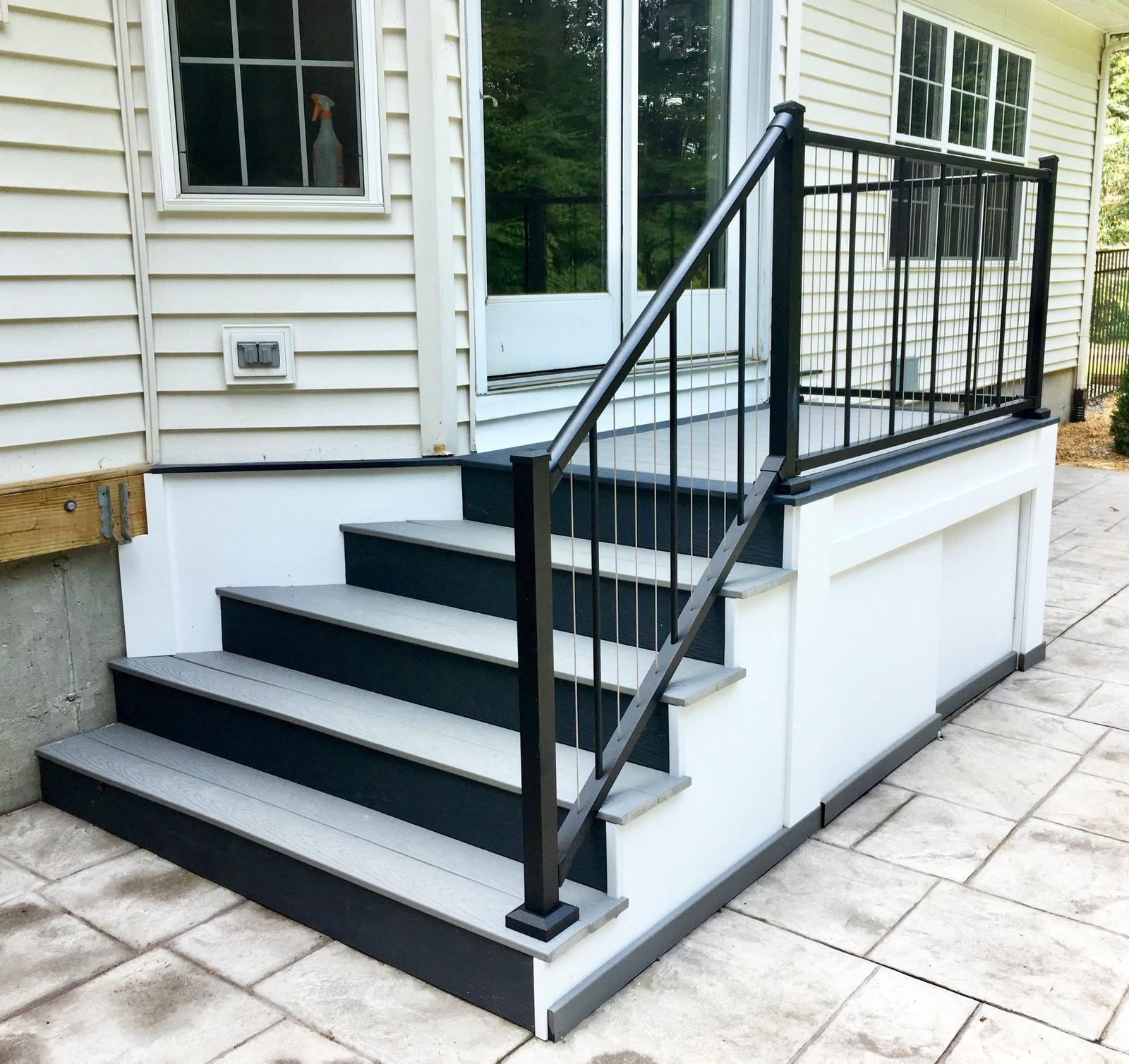 Composite stairs with white risers and black rail beside a stamped concrete patio