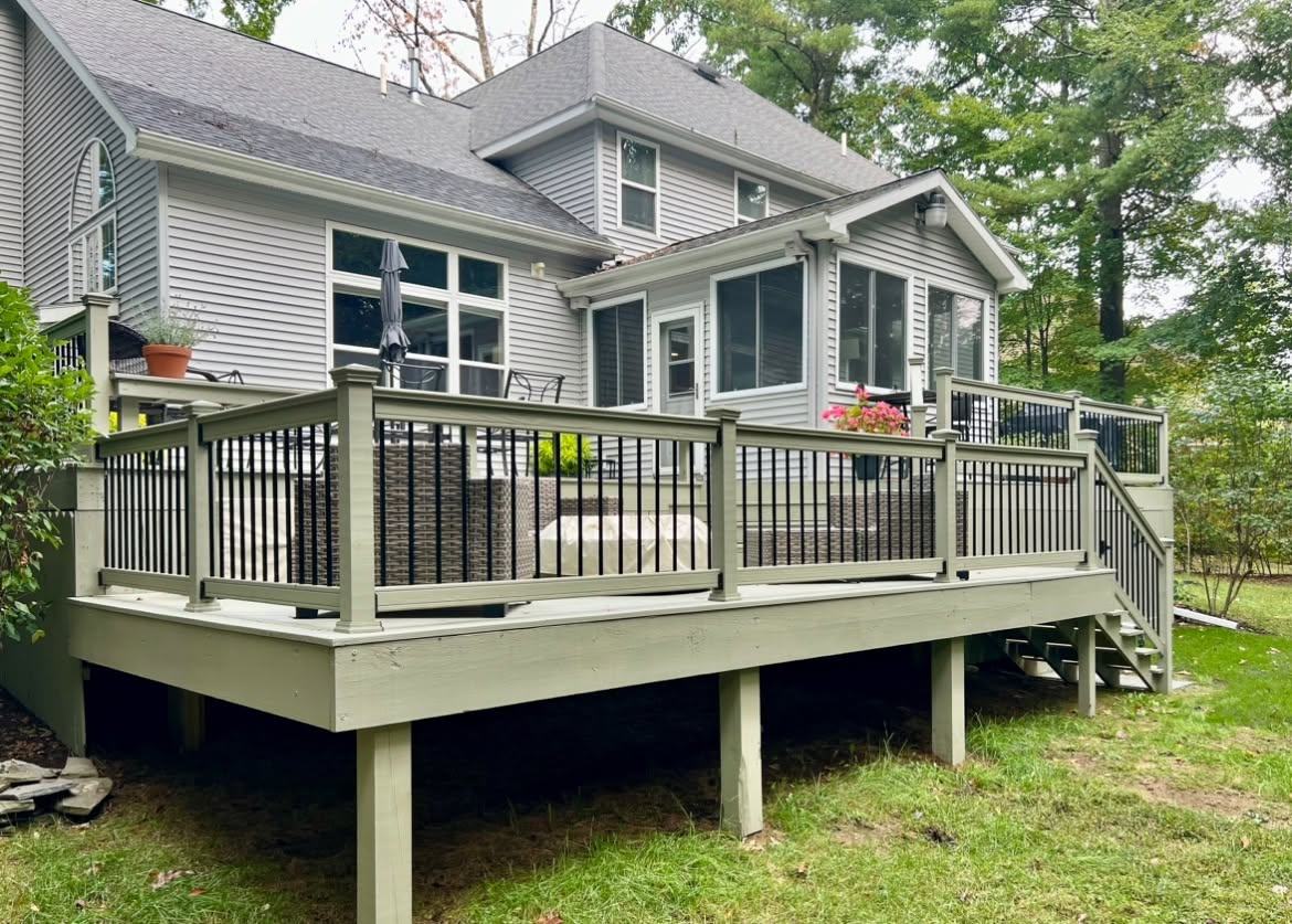 Rear of a gray house with a full-width deck, sage-painted rails and black balusters